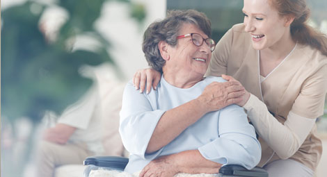Seated older woman with a younger carer stood to her side with a hand on her shoulder